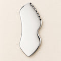 Stainless steel gua sha facial sculpting tool in a natural setting