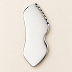 Stainless steel gua sha facial sculpting tool in a natural setting