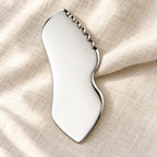 Stainless steel gua sha facial sculpting tool in a natural setting