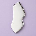Stainless steel gua sha facial sculpting tool in a natural setting