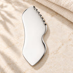 Stainless steel gua sha facial sculpting tool in a natural setting