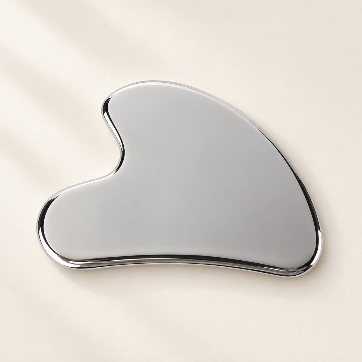 Silver wing-shaped gua sha on an ivory surface