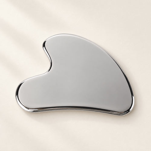 Silver wing-shaped gua sha on an ivory surface