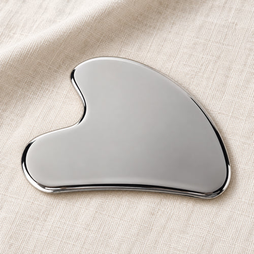 Silver wing-shaped gua sha in a natural self-care setting