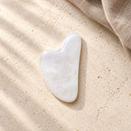 Gua Sha Facial Massage Stone - White in a wide natural setting with brown linen