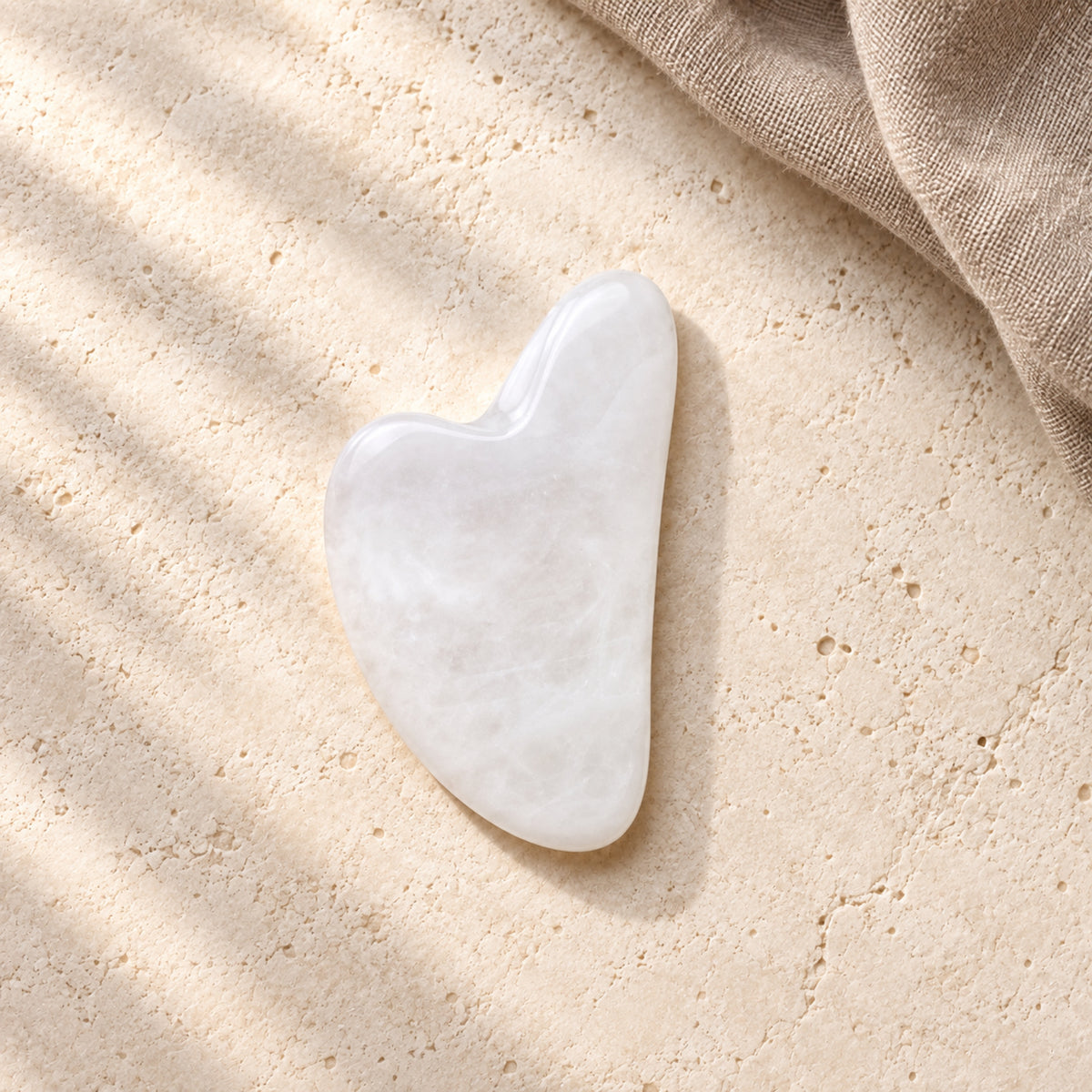 Gua Sha Facial Massage Stone - White in a wide natural setting with brown linen