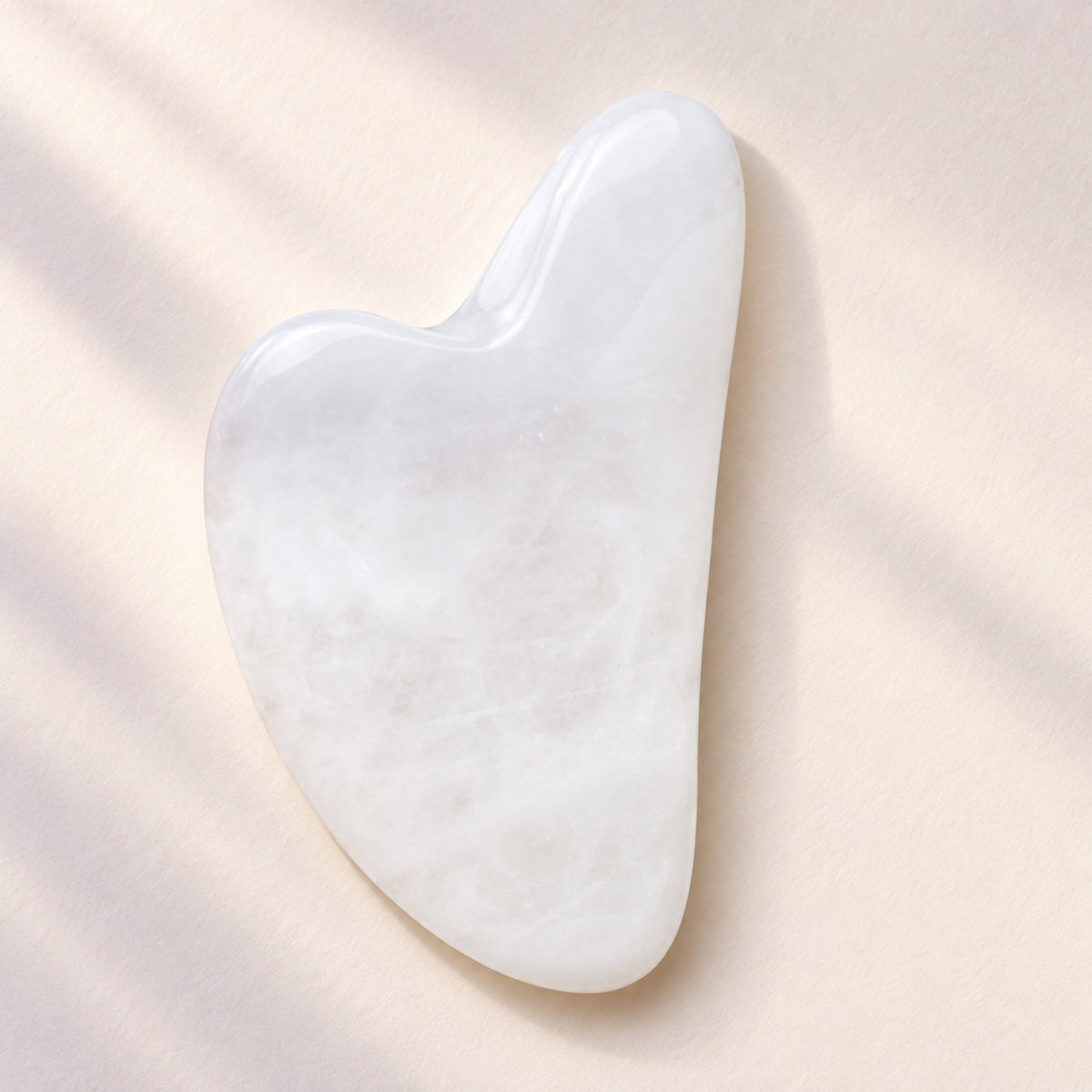 White jade gua sha facial massage tool on a soft neutral background